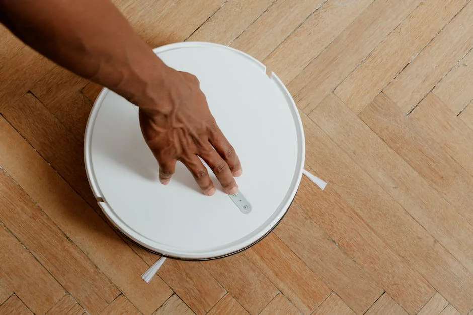 A close-up of a hand activating a robotic vacuum cleaner on a wooden floor. - affordable robotic vacuums for hardwood floors