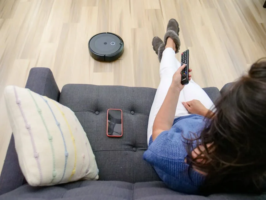 Person relaxing on a sofa controlling a robot vacuum cleaner with a remote. - affordable robotic vacuums for hardwood floors