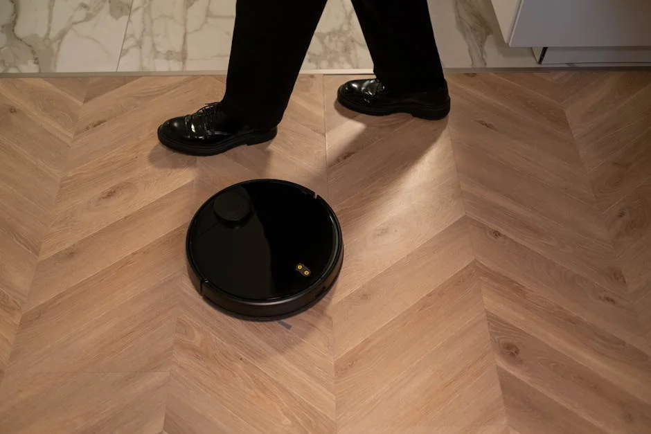 A modern robot vacuum cleaner navigating wooden floors while a person in black shoes walks past. - affordable robotic vacuums for hardwood floors