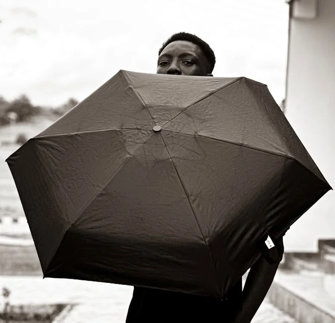 A person holding a large umbrella outdoors in a black and white photograph. - best compact umbrellas for windy weather