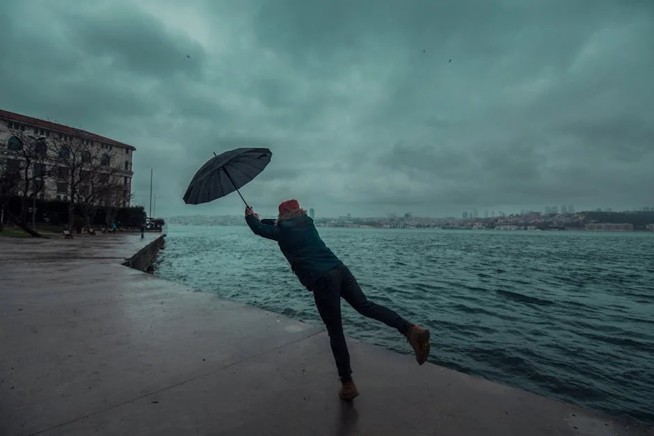 A man struggles with an umbrella near a stormy sea shore, capturing a windswept moment. - best compact umbrellas for windy weather