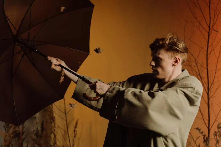 A fashionable man holds an umbrella against a windy autumn backdrop. Stylish pose. - best compact umbrellas for windy weather