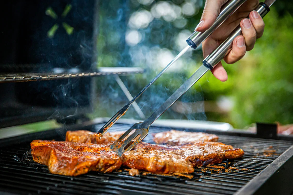 person holding gray tongs on barbecue - best meat thermometers for perfect grilling