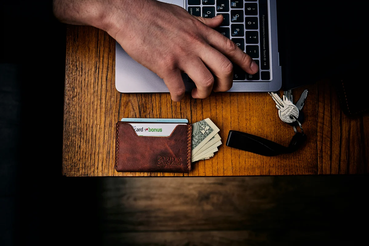 a person's hand on a wallet next to a laptop - best minimalist wallets for men with rfid blocking