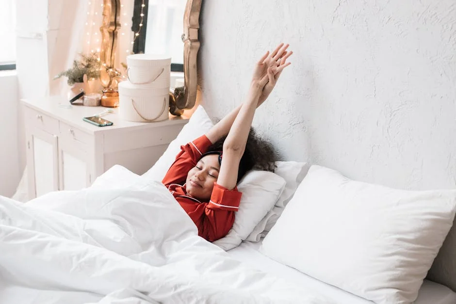 Woman in red pajamas stretching in a cozy, minimalist bedroom. Bright morning light enhances the serene scene. - rest relaxation bedroom - best organic cotton bed sheets for hot sleepers