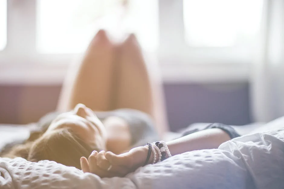 A woman lying on a bed in a peaceful, sunlit room, conveying relaxation. - rest relaxation bedroom - best organic cotton bed sheets for hot sleepers
