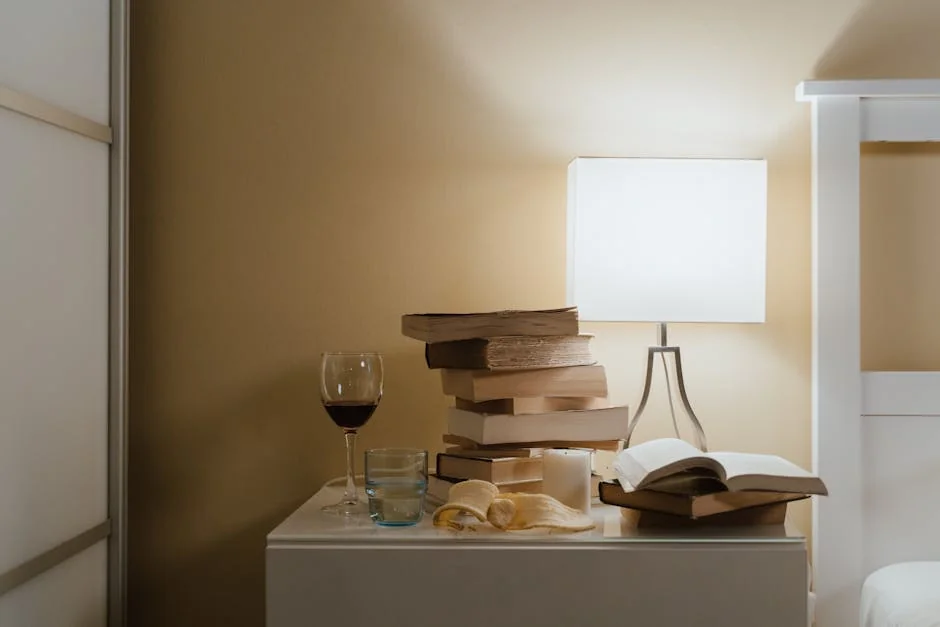 A minimalist bedroom nightstand with books, a lamp, and a glass of wine for a cozy evening vibe. - best reading lamps for bedside tables