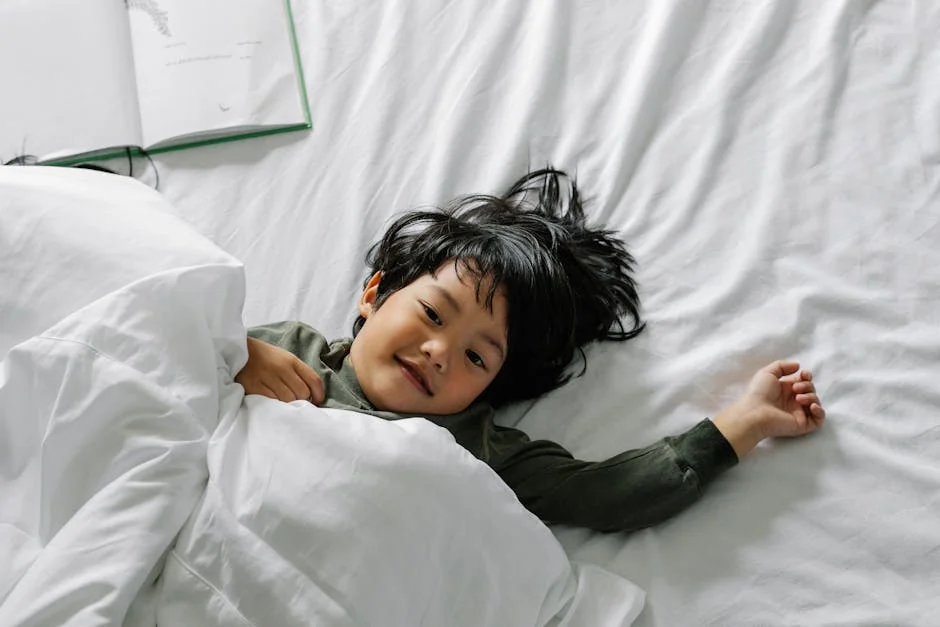 From above of relaxed Asian kid lying in comfortable bed under soft duvet in bedroom - best waterproof mattress protectors for kids