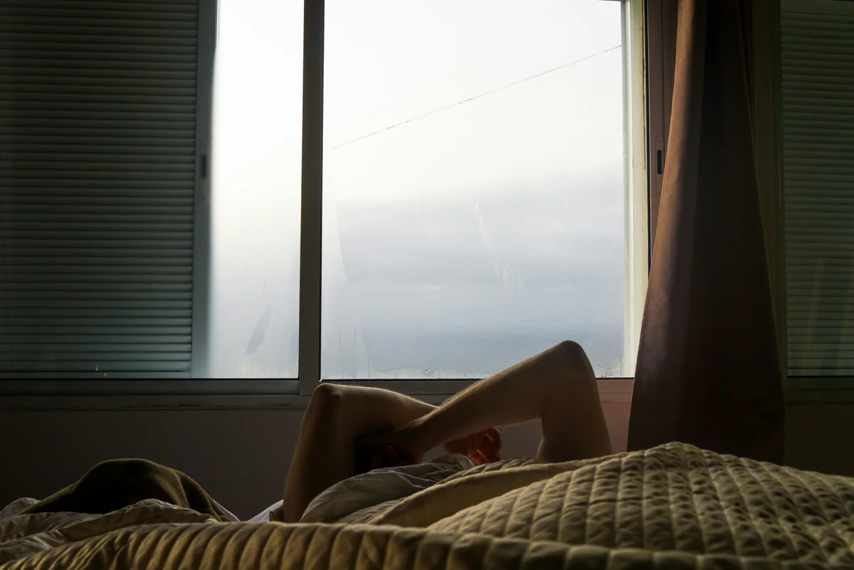 Person relaxing in bed with a window. - rest relaxation bedroom - best weighted blankets for anxiety and sleep
