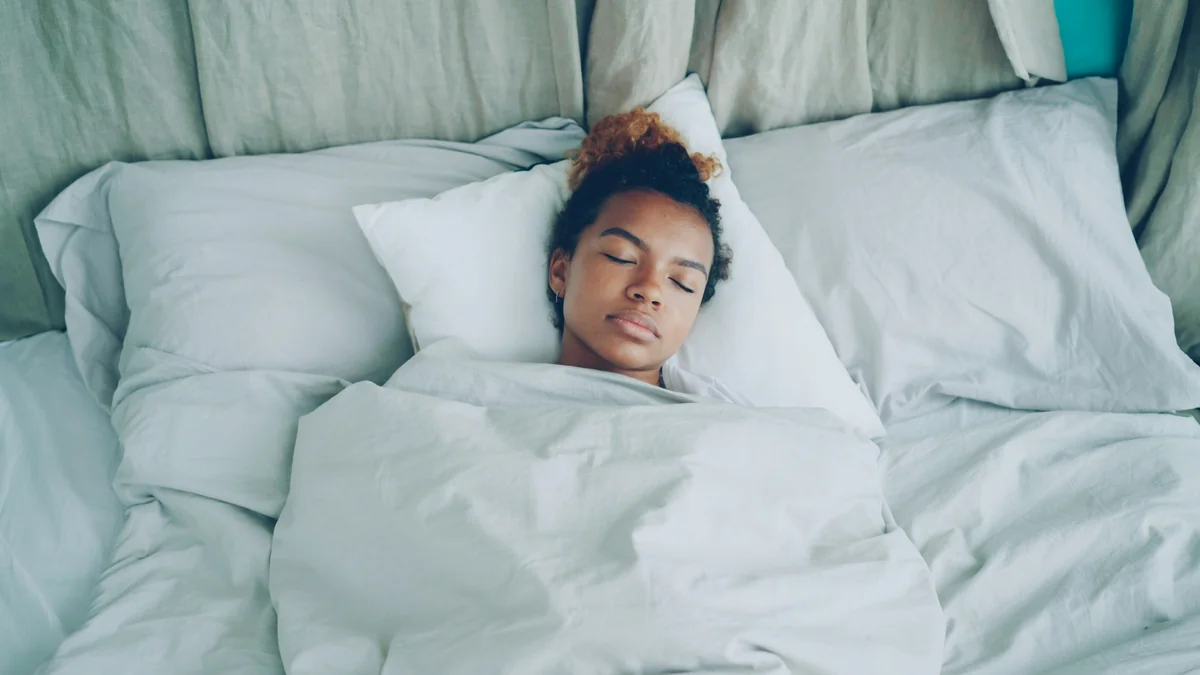 Young African American woman is sleeping in comfortable bed under warm blanket having rest on beautiful linen. Comfort, resting people and bedroom concept. - rest relaxation bedroom - best weighted blankets for anxiety and sleep