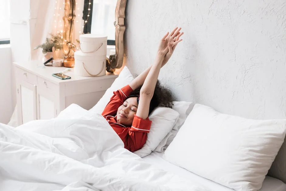 Woman in red pajamas stretching in a cozy, minimalist bedroom. Bright morning light enhances the serene scene. - rest relaxation bedroom - highly rated memory foam pillows for side sleepers
