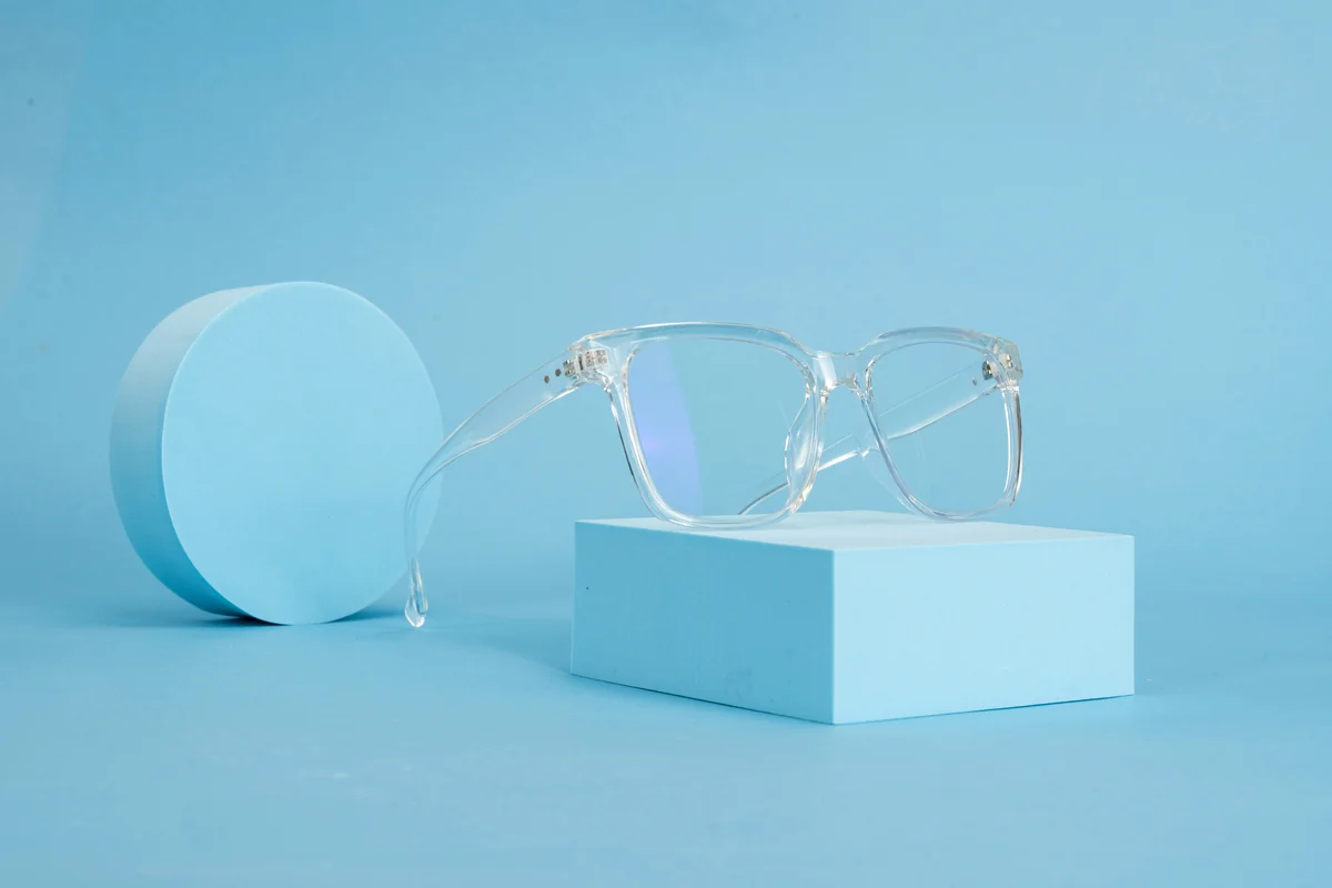 This image features a pair of clear eyeglasses stylishly displayed on a light blue rectangular block, against a matching blue background. The minimalist composition and monochromatic color scheme highlight the glasses' sleek, transparent design, making them stand out as a modern and fashionable accessory. - most stylish blue light blocking glasses for work