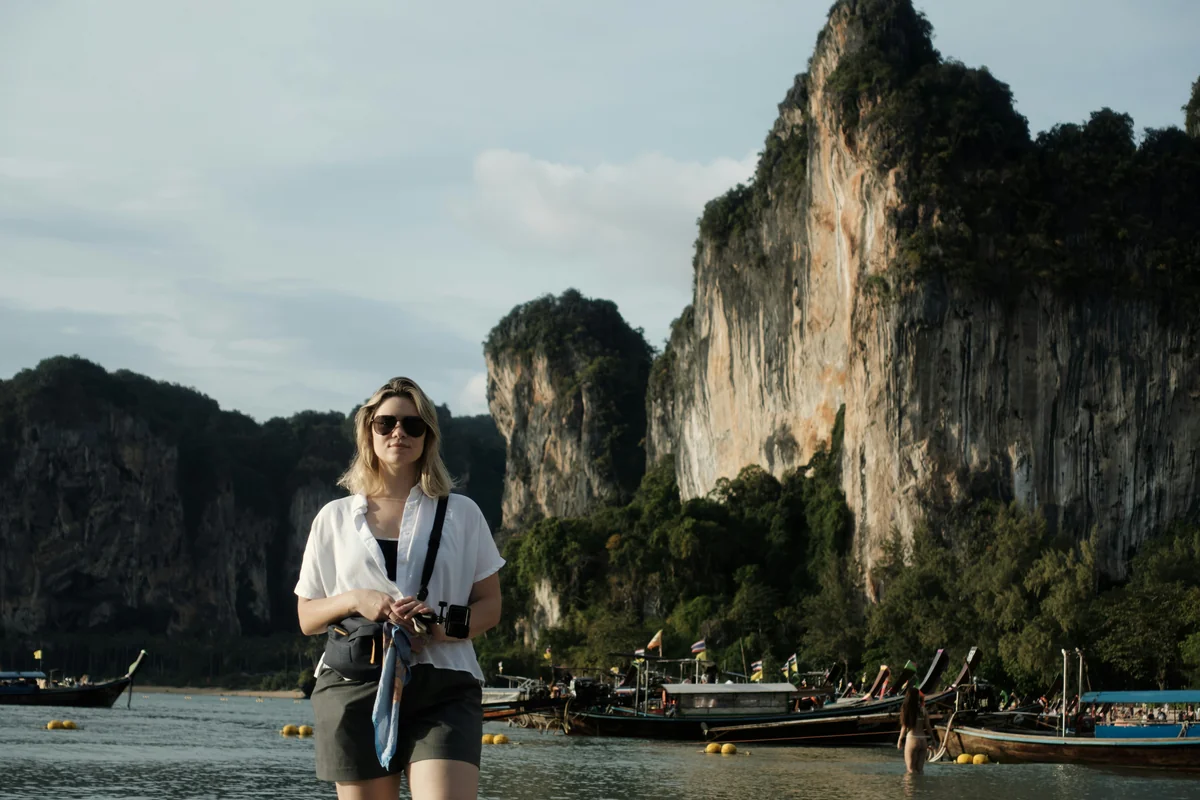 Woman with camera standing by ocean with boats and cliffs - adventure vacation destination - top rated handheld garment steamers for travel