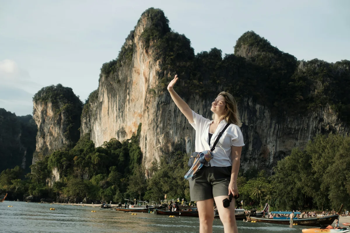 Woman raises hand against dramatic cliffs by the sea - adventure vacation destination - top rated handheld garment steamers for travel