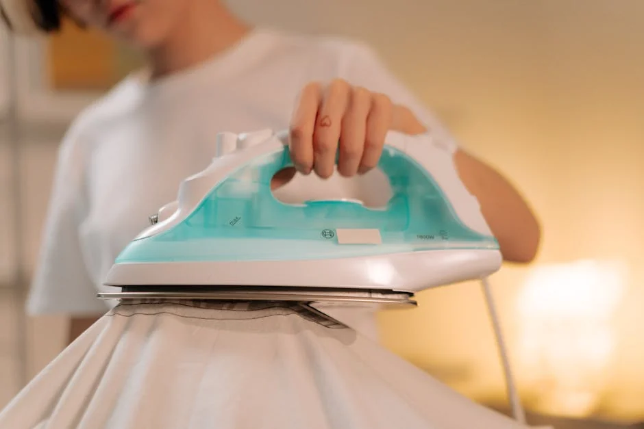 Close-up of a person using a steam iron for smoothing a white garment indoors. - top rated steam irons for professional results at home