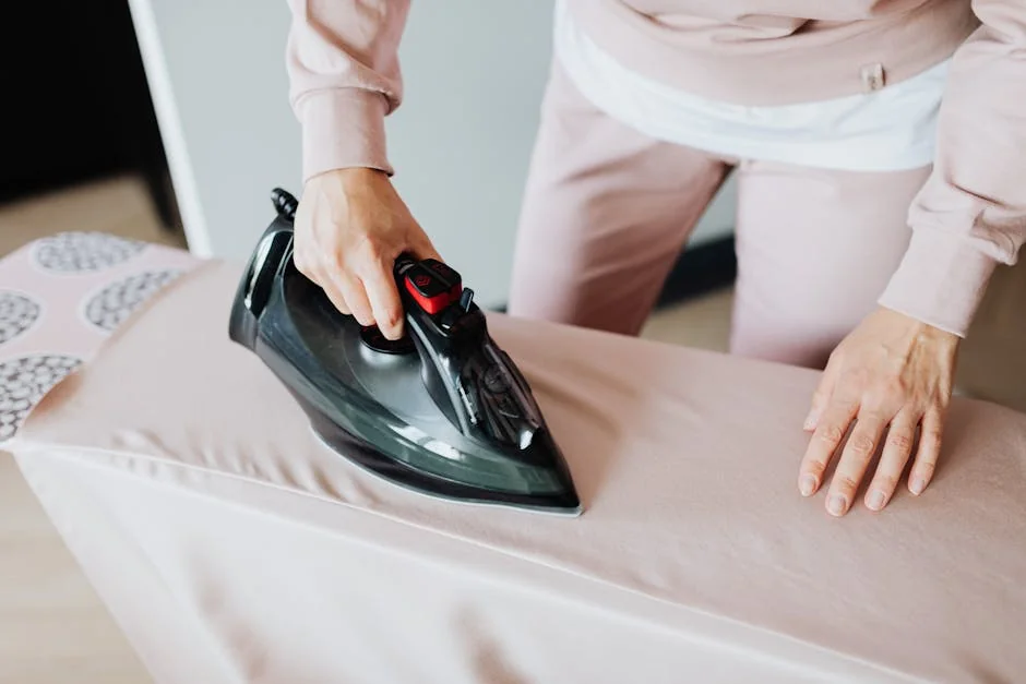 Adult woman ironing clothing on board using a black iron in an indoor setting. - top rated steam irons for professional results at home