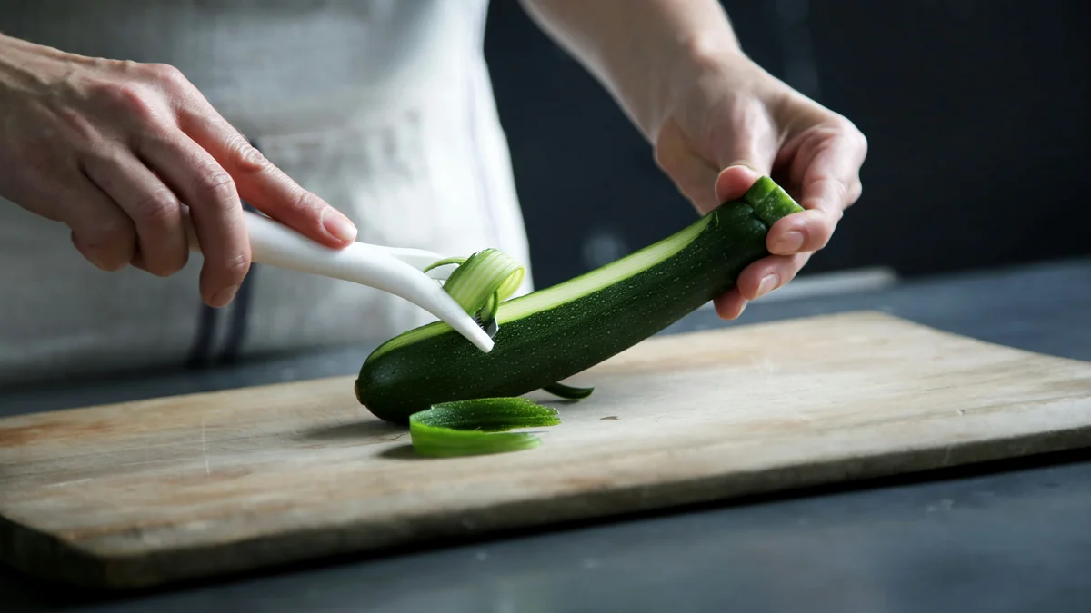 person pealing green cucumber inside room - top rated vegetable peelers for easy prep