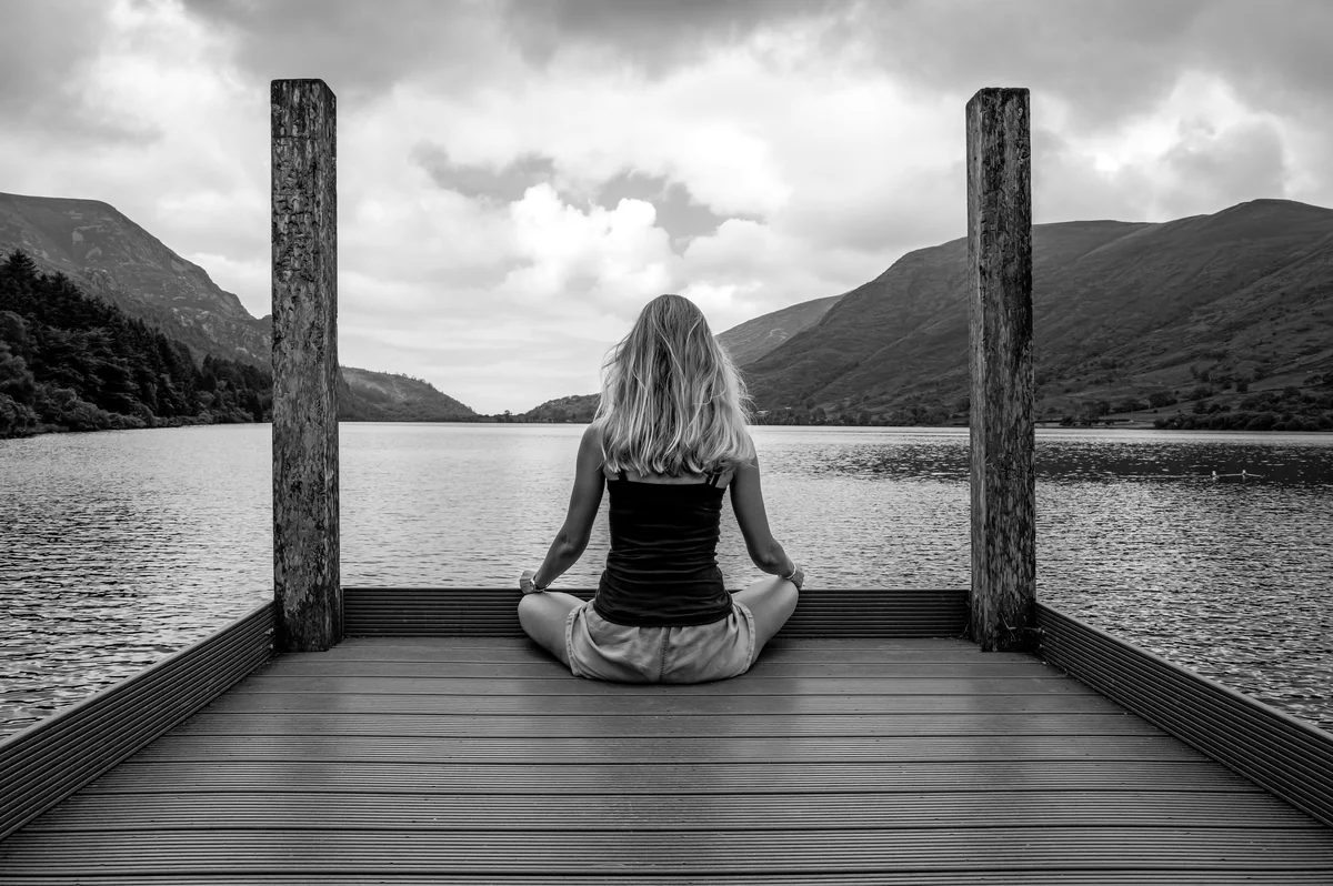 A woman sitting on a dock in front of a body of water - meditation wellness relaxation - top rated yoga mats for high intensity workouts
